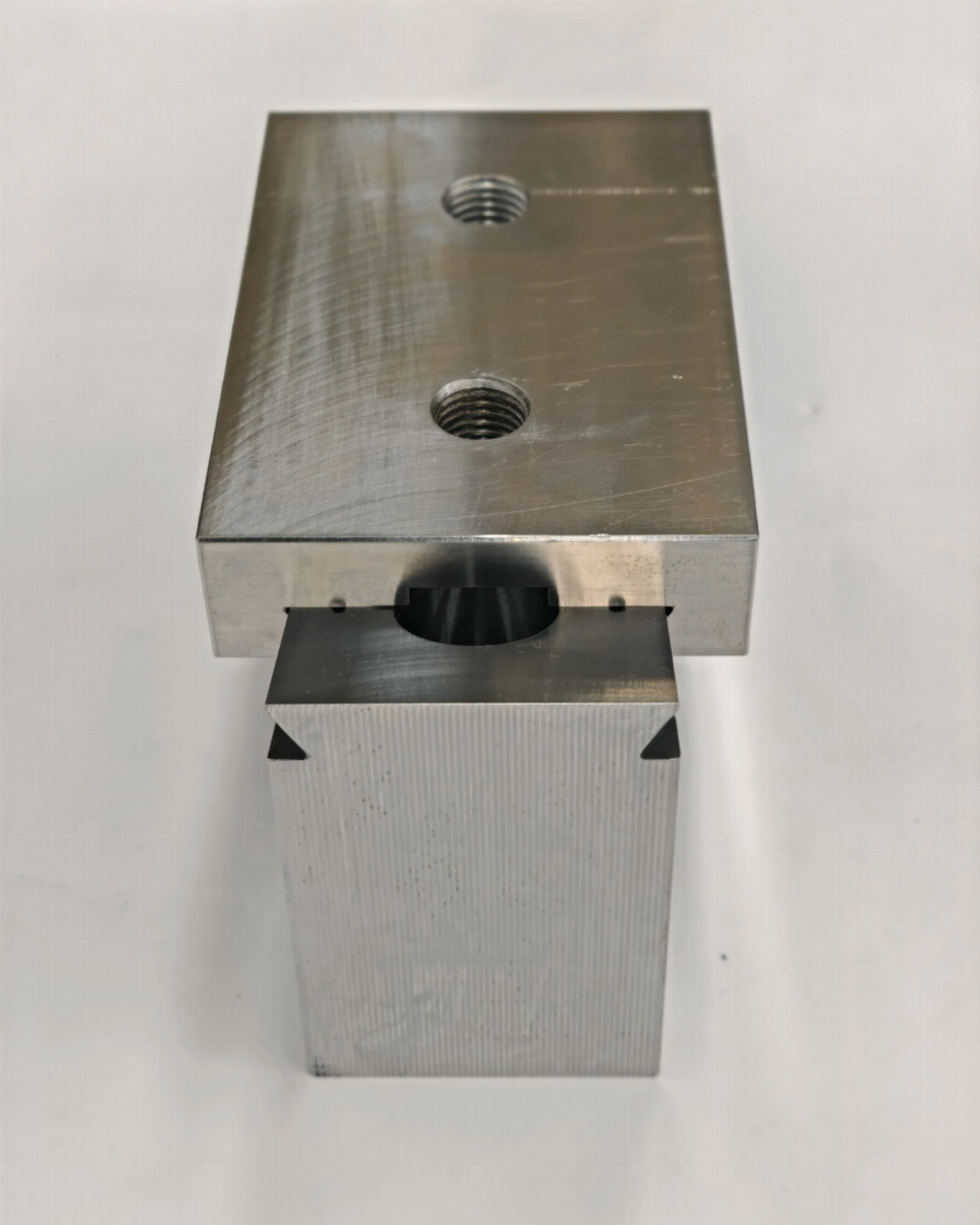 Imagen de detalle de una fresa CNC cortando una pieza de aluminio, con virutas de metal y fluido de corte visibles. La máquina y el entorno industrial están ligeramente desenfocados en el fondo.